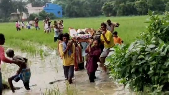A few villagers carrying bamboo canopies on their shoulders are walking towards the crematorium